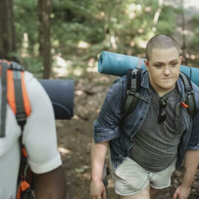 Diverse androgynous male backpackers trekking in lush forest