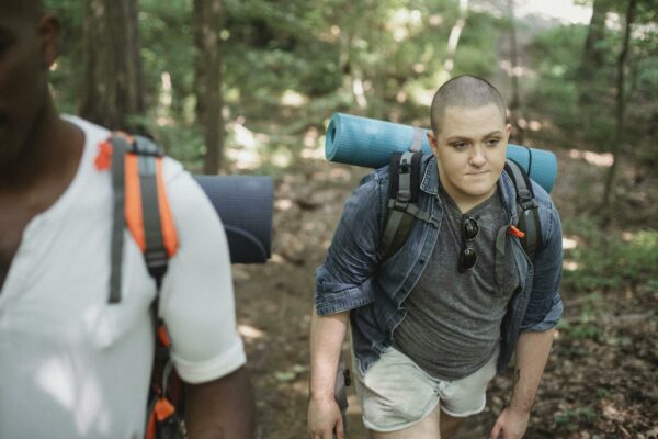 Diverse androgynous male backpackers trekking in lush forest