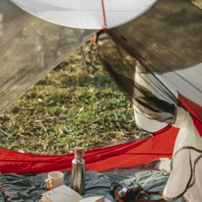 Spherical cam tent with opened book thermos bottle and modern photo camera placed on blanket in summer nature