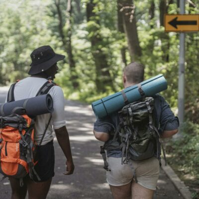 Unrecognizable diverse male hikers with backpacks walking along road